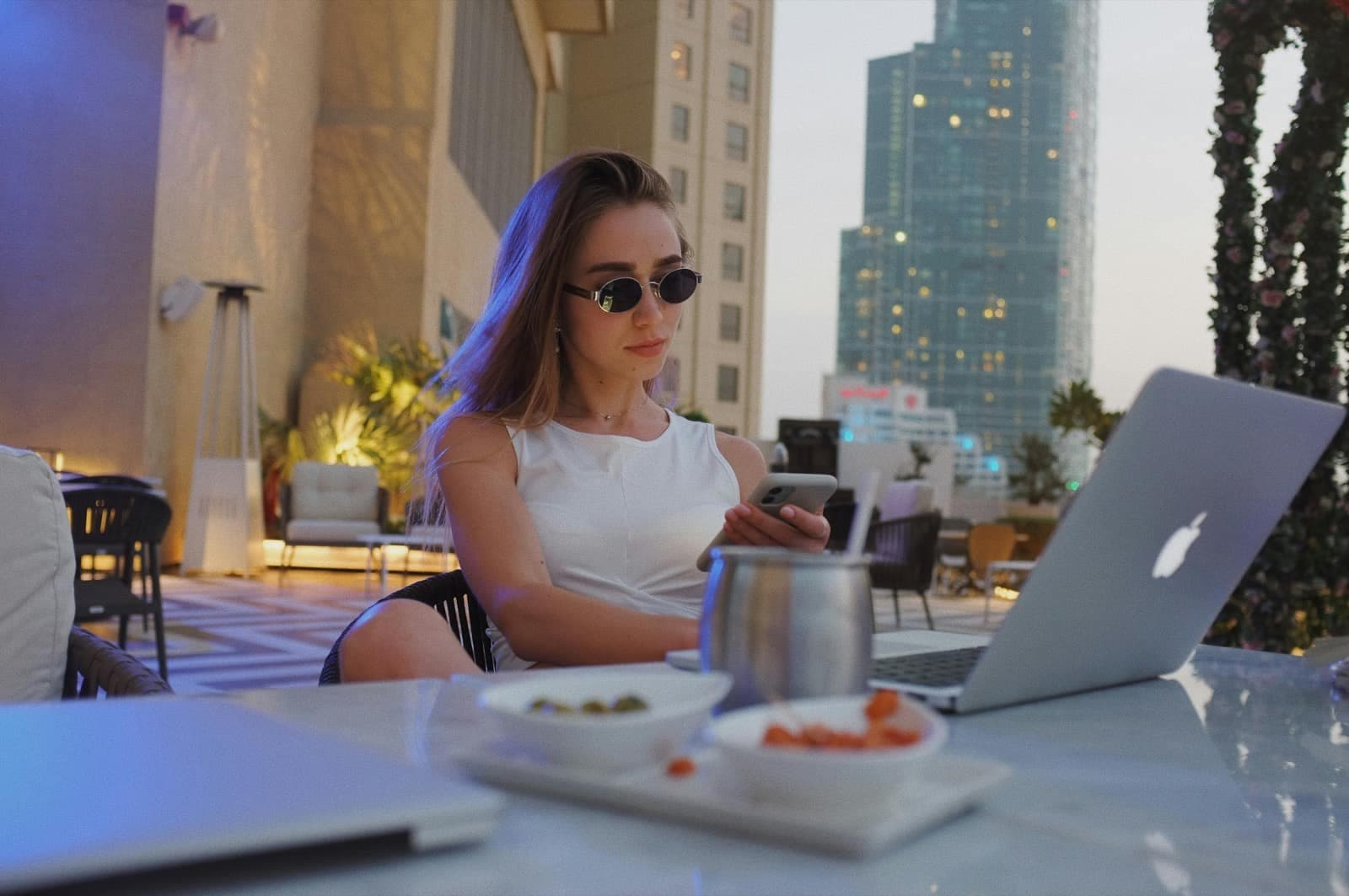 Bilgisayarının yanında telefonuna bakan bir kişi