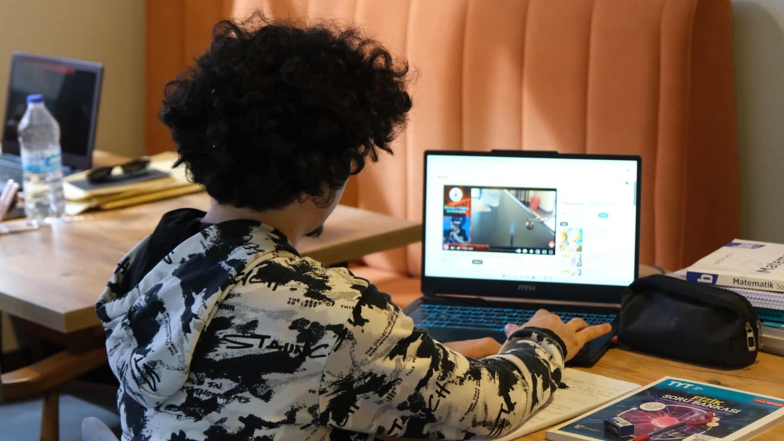 Kitaplarının yanında bilgisayardan ders videosu izleyen bir genç